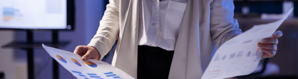 Em um escritório, uma mulher segurando duas folhas de papel com dashboards